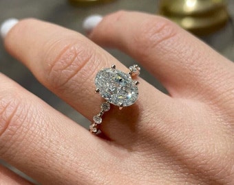 May include: A close-up of a ring featuring a large oval-shaped diamond set in a pave setting. The ring is worn on a person's finger.