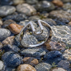 Peut inclure: Une bague ouverte de couleur argentée présentant une ouverture en forme de U sur le dessus. L'anneau est orné d'une rangée de petites pierres claires et scintillantes incrustées le long des bords extérieurs, suivant le contour de la bague.