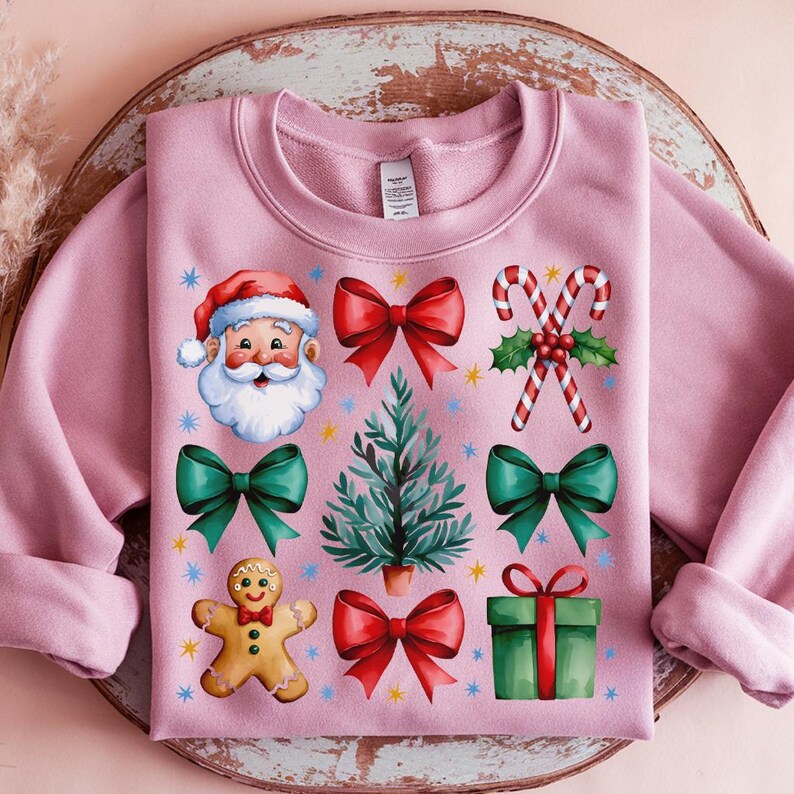 May include: Pink Christmas sweatshirt with a variety of festive designs including Santa Claus, a gingerbread man, a Christmas tree, candy canes, and bows.
