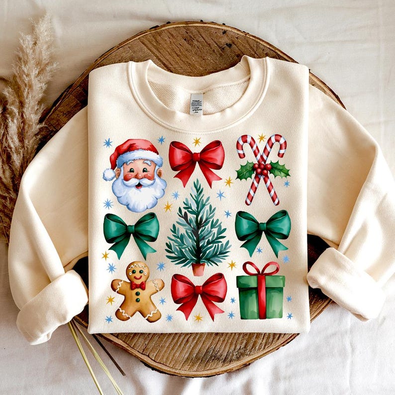 May include: A cream-colored sweatshirt with a Christmas theme. The design features Santa Claus, a Christmas tree, presents, candy canes, and gingerbread cookies.