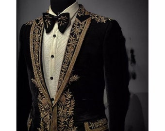 Puede incluir: Una chaqueta de terciopelo negro con bordados dorados. La chaqueta tiene un cuello chal y un cierre de un solo botón. El bordado presenta diseños florales.