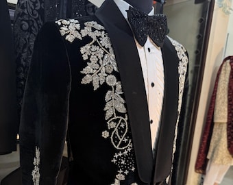 Puede incluir: Una chaqueta de terciopelo negro con bordados florales plateados. La chaqueta tiene un cuello chal y un cierre de un solo botón.