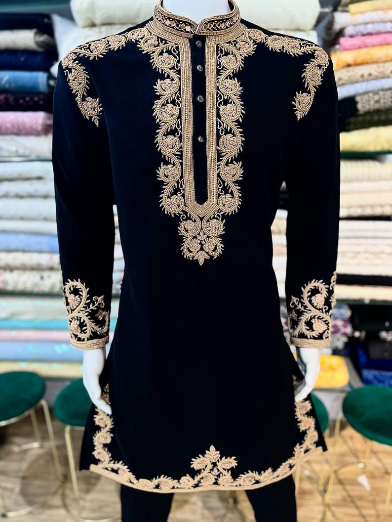 May include: A black tunic with elaborate gold embroidery. The long-sleeved garment showcases detailed floral and scrollwork patterns on the collar, cuffs, and front. It has a mandarin collar and a button-down front. The embroidery is ornate and adds a touch of sophistication.
