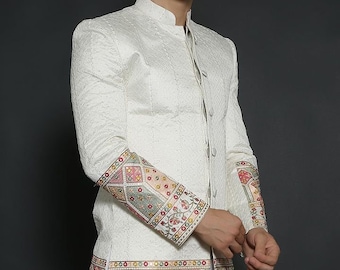 May include: A white long-sleeved jacket with a mandarin collar and button fastening. The jacket features intricate embroidery in shades of pink, green, and gold on the cuffs and hem.