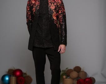 Puede incluir: Chaqueta negra con bordados florales rojos y naranjas, combinada con pantalones negros y zapatos marrones. La chaqueta tiene cuello mandarín y se lleva sobre una camisa negra. Un atuendo formal.