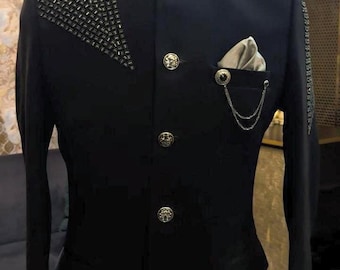 May include: Black formal jacket with gold buttons and decorative detailing. The jacket has a mandarin collar and a pocket square with a chain. The word "ENIGMA" is visible on the collar.