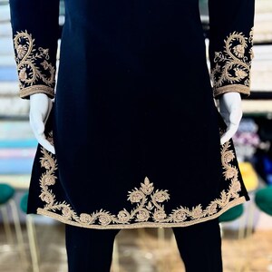 May include: Black tunic with gold embroidery. The tunic has detailed gold floral embroidery on the cuffs, hem, and upper chest. The sleeves are long, and the tunic has a straight, slightly A-line shape. The garment is displayed on a mannequin.
