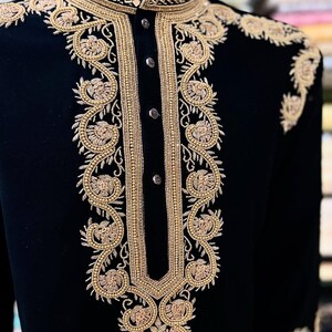May include: A black velvet jacket with detailed gold embroidery. The jacket has a mandarin collar and elaborate floral patterns on the front, shoulders, and cuffs. The gold embroidery includes small beads, giving a luxurious and formal look.
