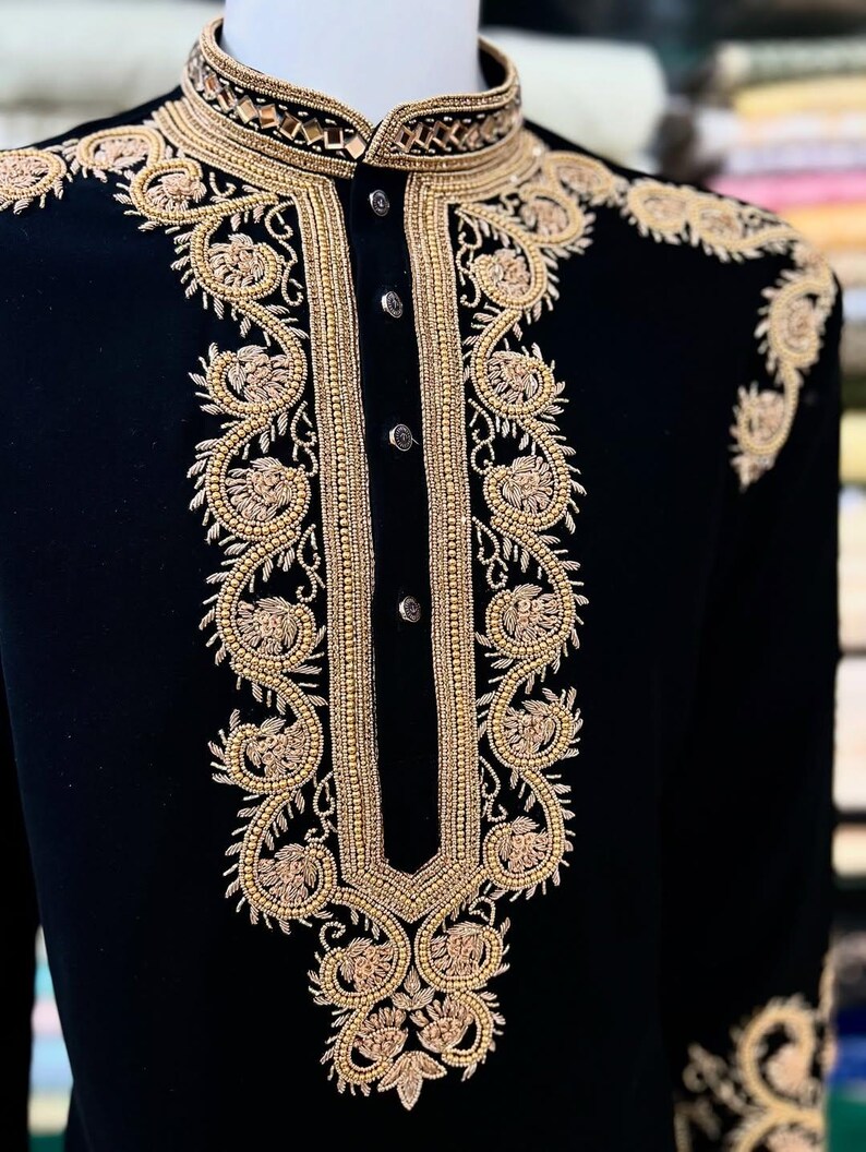 May include: A black velvet jacket with detailed gold embroidery. The jacket has a mandarin collar and elaborate floral patterns on the front, shoulders, and cuffs. The gold embroidery includes small beads, giving a luxurious and formal look.