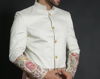 May include: A white blazer with a mandarin collar and gold buttons. The blazer has a patterned trim around the cuffs and bottom hem.