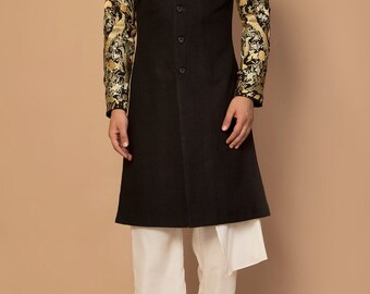Könnte beinhalten: Eine schwarze, langärmelige Kurta mit goldenen und schwarzen Stickereien an den Ärmeln. Die Kurta wird mit einer weißen Hose und schwarzen Schuhen kombiniert.