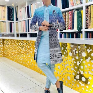 May include: A light blue long-sleeved jacket with a black and white patterned design. The jacket has a mandarin collar and a button closure. The person is wearing light blue pants and black shoes.