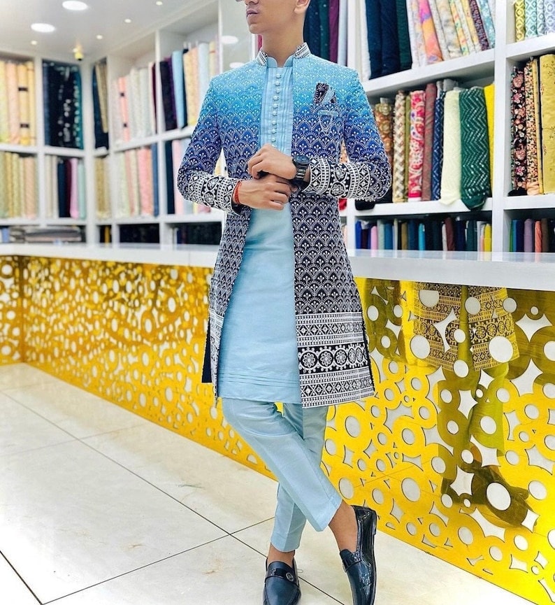 May include: A light blue long-sleeved jacket with a black and white patterned design. The jacket has a mandarin collar and a button closure. The person is wearing light blue pants and black shoes.
