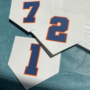 May include: Three white baseball home plate-shaped cards with blue numbers 1, 2, and 7. The numbers have an orange outline.