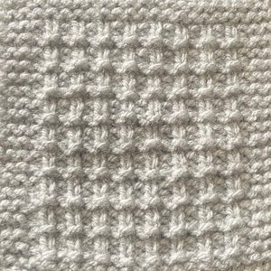 May include: A close-up of a silver knitted fabric with a textured pattern. The fabric is soft and fluffy, and the texture is created by the way the yarn is woven together.