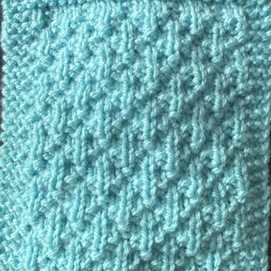 May include: A square, hand-knitted item in a light blue colour. The knitted texture features a repeating pattern of vertical and diagonal lines, creating a textured surface. The edges are neatly finished with a border.