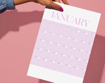 Könnte beinhalten: Eine Kalenderseite für Januar 2026, gehalten von einer Hand. Der Kalender hat ein hellviolettes Raster auf weißem Hintergrund, mit dem Monatsnamen in einer passenden violetten Schriftart. Das Jahr 2026 befindet sich in der unteren rechten Ecke. Die Hand hat rosa Nagellack.