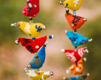 May include: Two vertical hanging garlands featuring a series of stuffed fabric bird ornaments in various colors including red, yellow, blue, orange, and green. Each bird is decorated with printed patterns, small sequins, and tiny metallic bells.