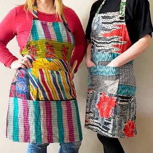May include: Two colorful patchwork aprons with different patterns and designs. Both aprons have pockets and are made from recycled fabric.