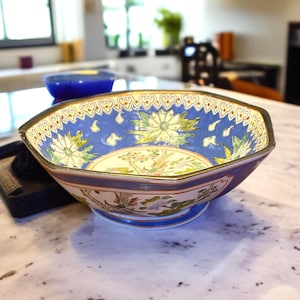 May include: An octagonal ceramic bowl with a blue interior and a gold rim. The bowl features floral and bird designs in shades of yellow, green, and pink. The exterior is a deep blue with a cream-colored band.