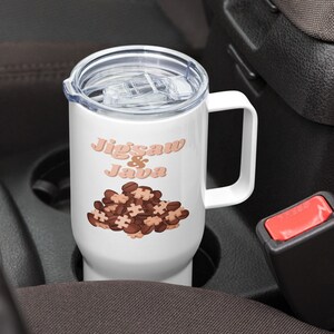 Op de afbeelding: Witte reistumbler met een deksel en een handvat. De tumbler heeft een ontwerp van bruine puzzelstukjes met de tekst "Jigsaw & Java" in roze.