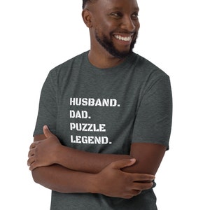 May include: A dark heather grey t-shirt with white text that reads "Husband. Dad. Puzzle Legend."