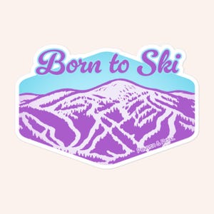 May include: A sticker with a purple mountain scene and the words "Born to Ski" in a script font. The sticker has a light blue and purple color scheme, with the text in a light purple color. The brand name "Powder & Petal" is at the bottom.