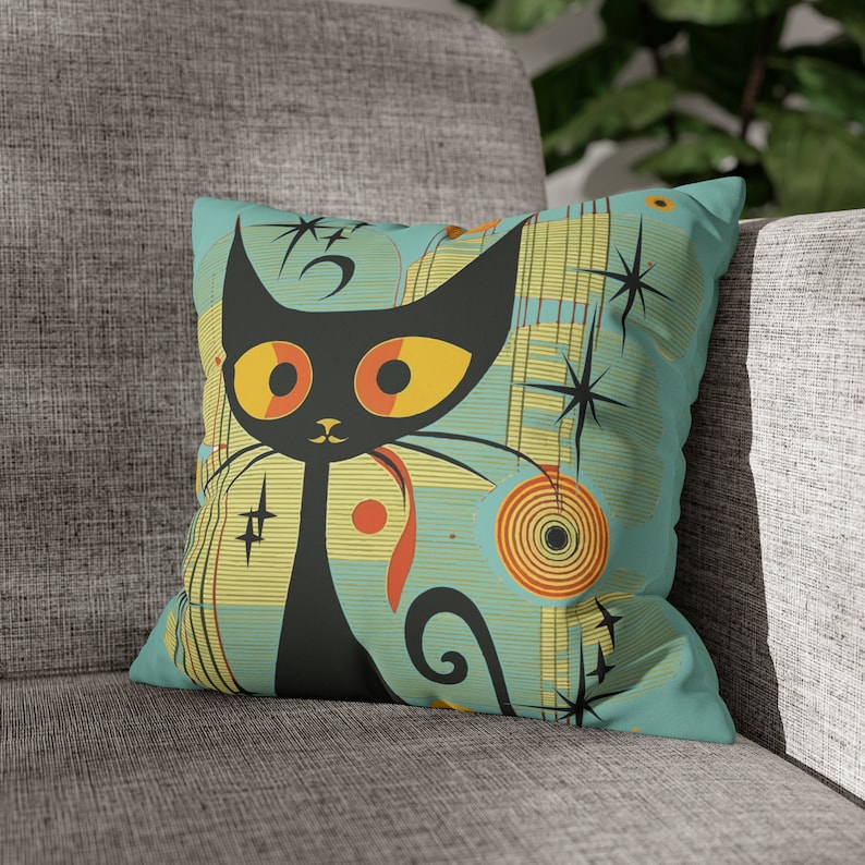May include: A turquoise blue throw pillow with a black cat illustration. The cat has large yellow eyes and a red tongue. The background features a retro-style pattern with yellow, orange, and white geometric shapes.