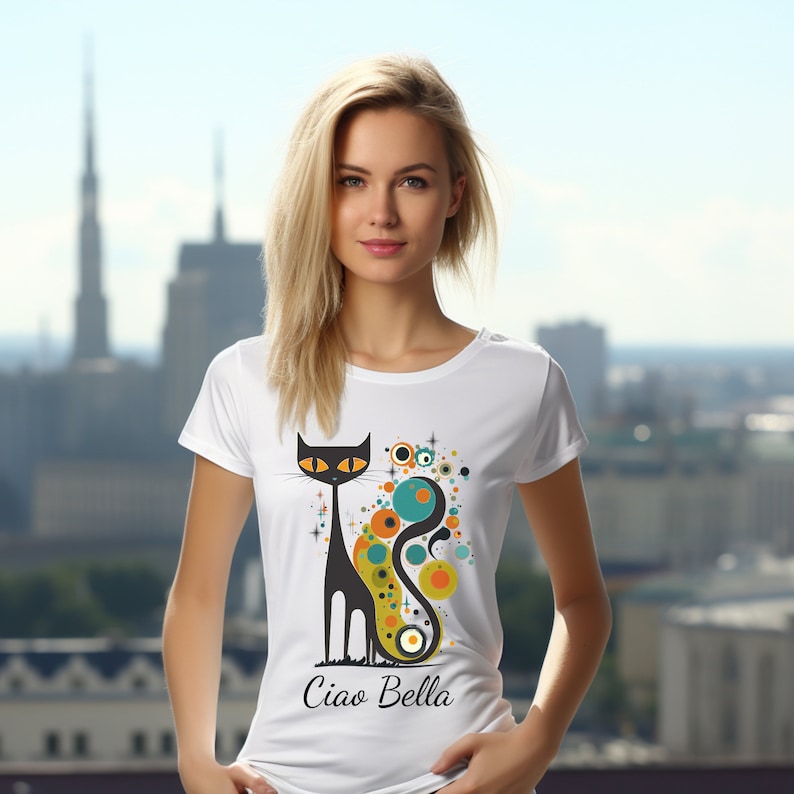 May include: White t-shirt featuring a stylized black cat design with orange eyes and a long tail, accented by colorful circles and stars. The text "Ciao Bella" is printed below the cat. The shirt is a classic crew neck.