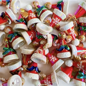 May include: A collection of red and white Santa hats with snowflake designs and iridescent accents. The hats have white fur trim and are scattered across a white surface. Some hats have green bows and small faces.