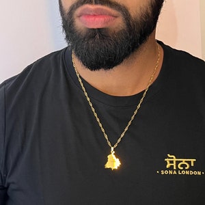 Op de afbeelding: Een goudkleurige ketting met een hanger in de vorm van een kaart. De ketting wordt gedragen over een zwart t-shirt met gouden tekst "SONA LONDON". De hanger is een gedetailleerde omtrek van een geografische regio.