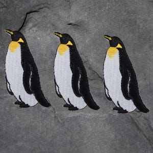 May include: Three embroidered penguin patches with black and white bodies, yellow beaks, and black eyes. The patches are on a gray background.