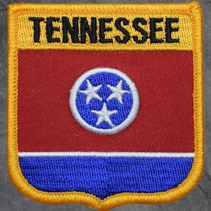 May include: Embroidered patch featuring the word "TENNESSEE" in black on a yellow banner. Below, a red field with a blue and white emblem of three stars is set above a blue base, all framed by a yellow border.