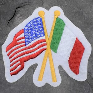 May include: Embroidered patch featuring the flags of the United States and Italy crossed. The American flag has red and white stripes with a blue field of white stars. The Italian flag is green, white, and red. The patch has a white border.