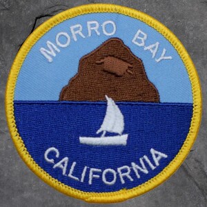 May include: Circular patch featuring a brown rock formation, a sailboat, and the text "MORRO BAY CALIFORNIA". The patch has a blue sky and sea, with a yellow border.