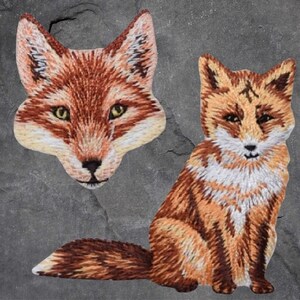 May include: Two embroidered fox patches. One is a close-up of a fox's face, the other is a full-body fox sitting with its tail curled around its legs.