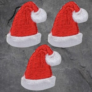 May include: Three red and white felt Santa hats with white pom-poms. The hats are approximately 5 cm tall.