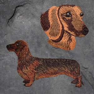 May include: Two embroidered dachshund dog patches. One is a brown and black dachshund with its head turned to the side. The other is a brown and black dachshund lying down.