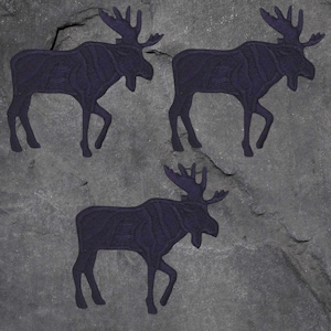 May include: Three dark blue moose silhouettes are arranged on a gray, textured background. The moose are depicted in a walking pose, with detailed antlers. The image has a rustic, outdoorsy feel.