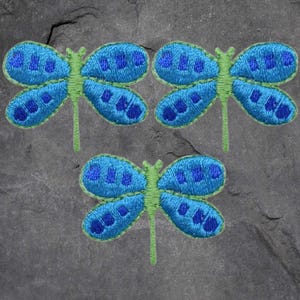 May include: Three blue and green embroidered dragonfly appliques. The dragonflies have a light blue body with dark blue spots and green wings.
