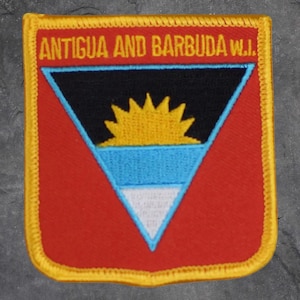 May include: A rectangular patch with a red background and a yellow border. The patch features the text "ANTIGUA AND BARBUDA W.I." in orange. Inside is a triangle with a black top, yellow sun, blue and white sections.