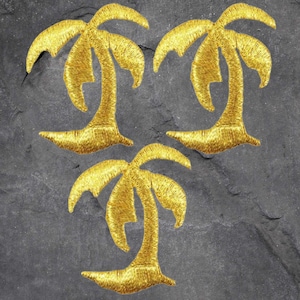 May include: Three gold embroidered palm tree iron-on patches. The palm trees are a simple silhouette design with a curved trunk and fronds.