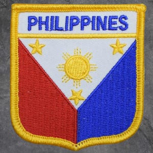 May include: Embroidered patch featuring the word "PHILIPPINES" in blue above a shield design. The shield is divided into red, white, and blue sections, with three yellow stars and a yellow sun emblem. The patch has a yellow border.