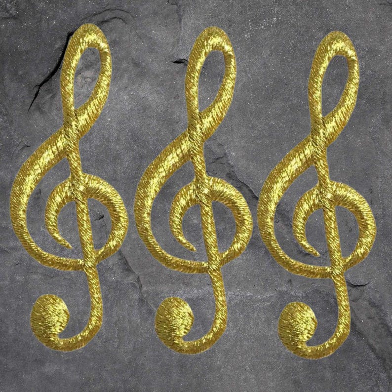 Puede incluir: Tres parches dorados con forma de clave de sol sobre un fondo de piedra gris. Los s&iacute;mbolos musicales est&aacute;n bordados con un hilo texturizado y met&aacute;lico, creando un efecto brillante. Ideal para amantes de la m&uacute;sica y artesanos.