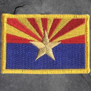 May include: Embroidered patch featuring the Arizona state flag. The design includes a blue lower section, a red and yellow sunburst, and a gold star in the center. The patch has a yellow border.
