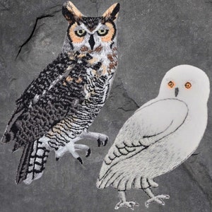 May include: Two embroidered owl patches. One is a brown and black great horned owl with orange eyes. The other is a white snowy owl with orange eyes.