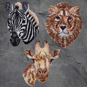 May include: Three embroidered iron-on patches featuring animal faces: a zebra, a lion, and a giraffe. The patches are brown, black, and white.