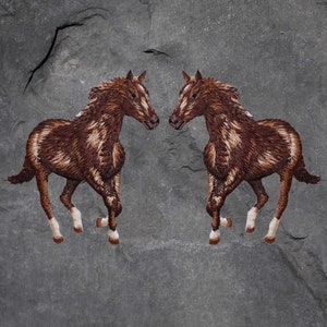 May include: Two brown and white horses facing each other, embroidered on a grey stone background.