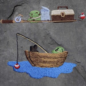 May include: Embroidered design of a fishing scene with a boat, a fishing rod, and a bobber. The boat is brown and has a green figure sitting in it. The fishing rod is brown and has a green bobber at the end. The scene is set against a gray background.
