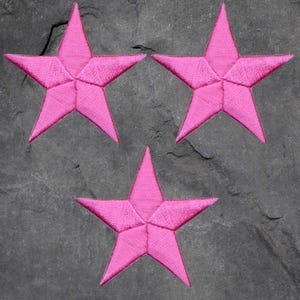 May include: Three pink fabric stars on a grey background. The stars are five-pointed and have a slightly textured surface.
